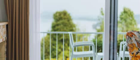A room with a balcony, a dining table with a hat and fruit, and two wine glasses.