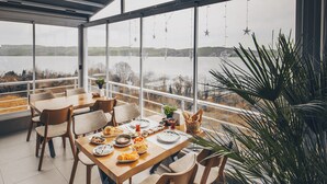 A dining area with a large table and chairs, a potted plant, and a view of a lake.
