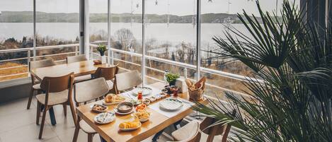 A dining area with a large table and chairs, a potted plant, and a view of a lake.