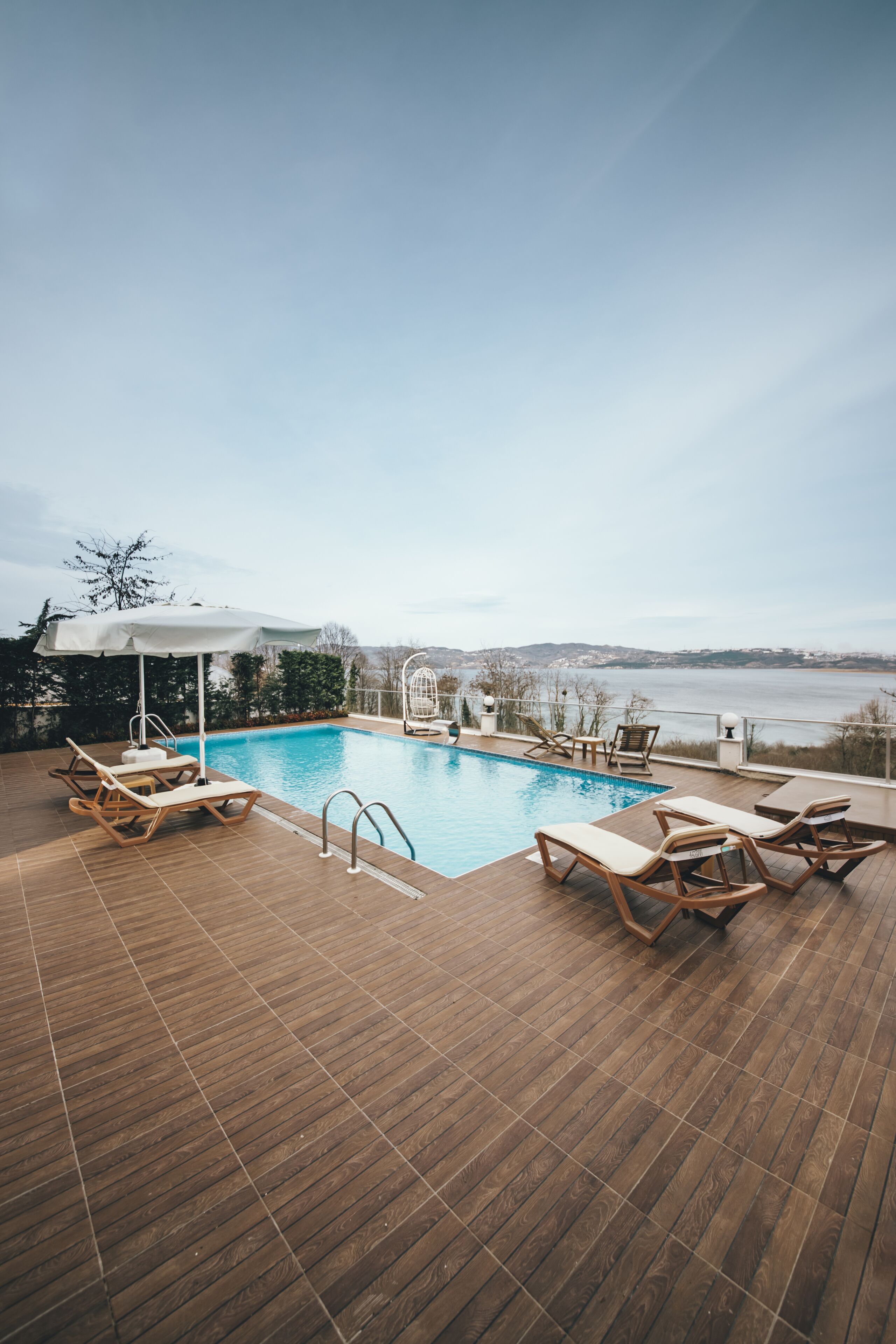 A wooden deck with a pool, lounge chairs, and a view of the water.