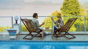 Two people relaxing by a poolside with a view of a lake and distant buildings.