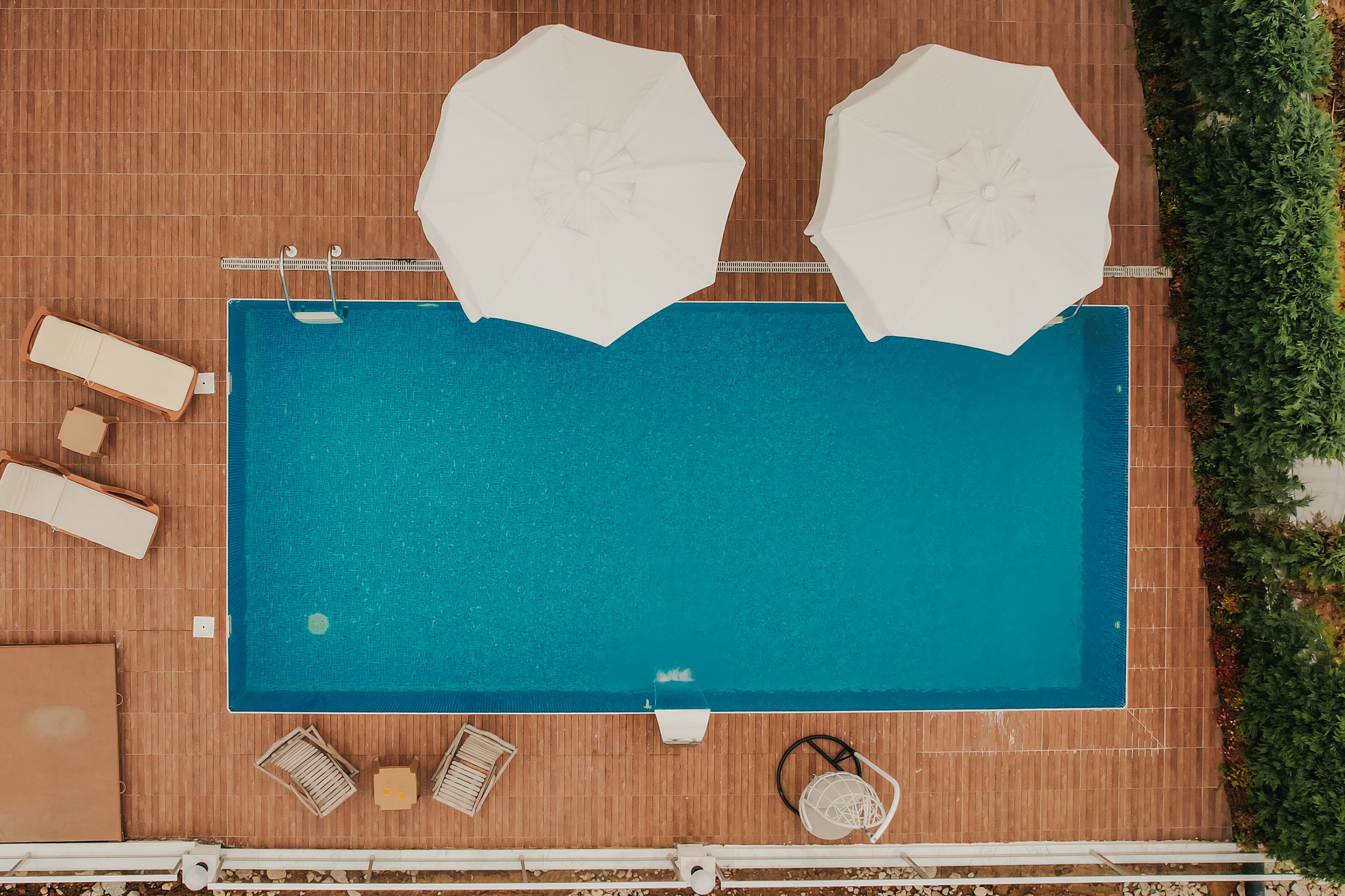 Luchtbeeld van een zwembad met twee parasols, lounge stoelen en een ligbed op een houten terras.