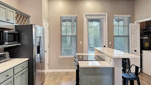 A modern kitchen with a refrigerator, microwave, and stove, a bar area, and large windows. - Lite House II at Martinique - Golf Cart Included - Just steps to the beach!!! (Fort Morgan)