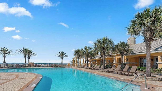 A swimming pool with lounge chairs and palm trees, surrounded by a building with a yellow facade. - Lite House II at Martinique - Golf Cart Included - Just steps to the beach!!! (Fort Morgan)