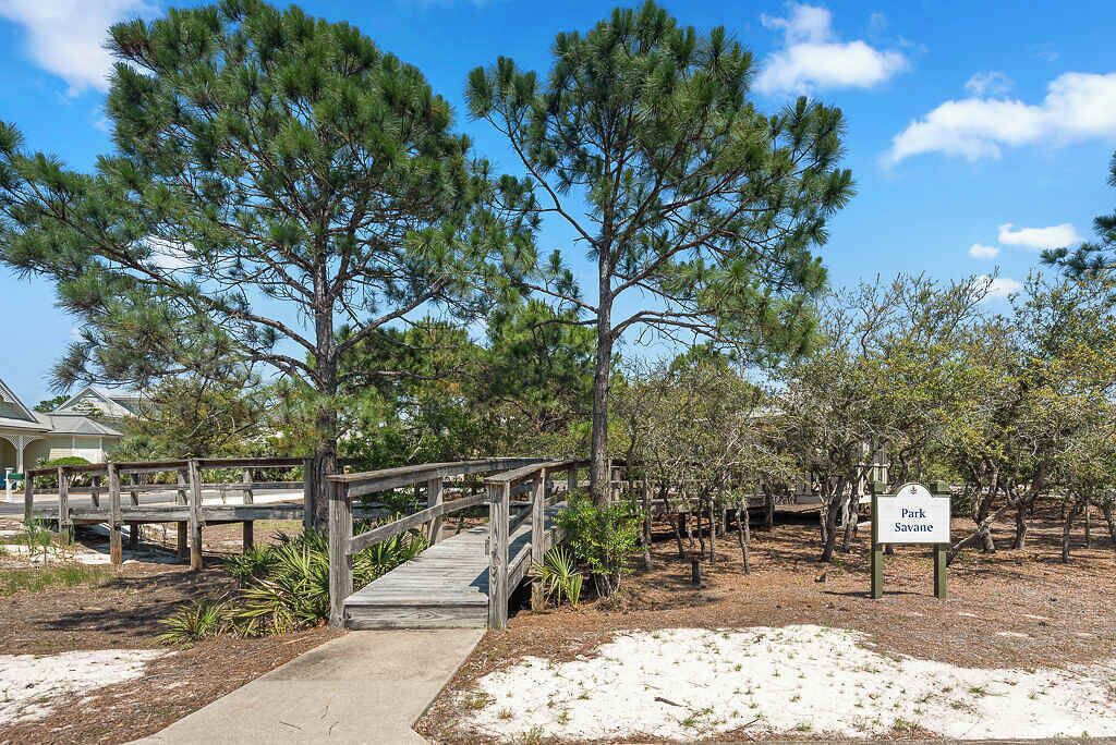 A wooden bridge leading to a park area with a sign reading "Park Savane".