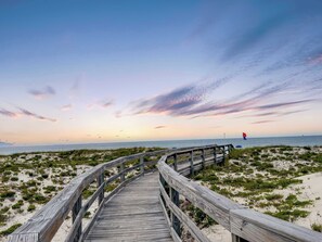 A wooden boardwalk leading to a beach with sparse vegetation and a clear sky. - Lite House II (Fort Morgan)