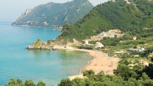 Eine Küstenlandschaft mit Strand, Felsen und Bergen im Hintergrund.