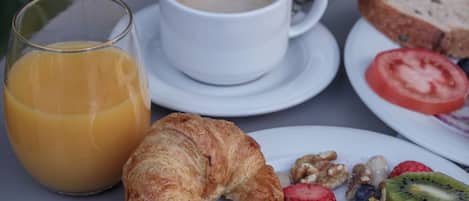 A breakfast setting with a croissant, fruit, pancakes, a glass of orange juice, and a cup of coffee on a table.