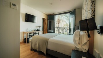 Quarto de hotel com cama, escrivaninha, televisão e janela com vista para palmeiras.