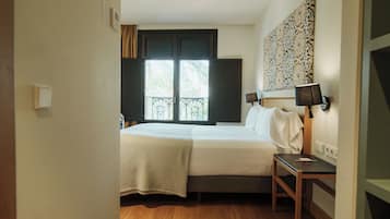 Un dormitorio con cama, mesita de noche, lámpara y ventana con vistas a palmeras.
