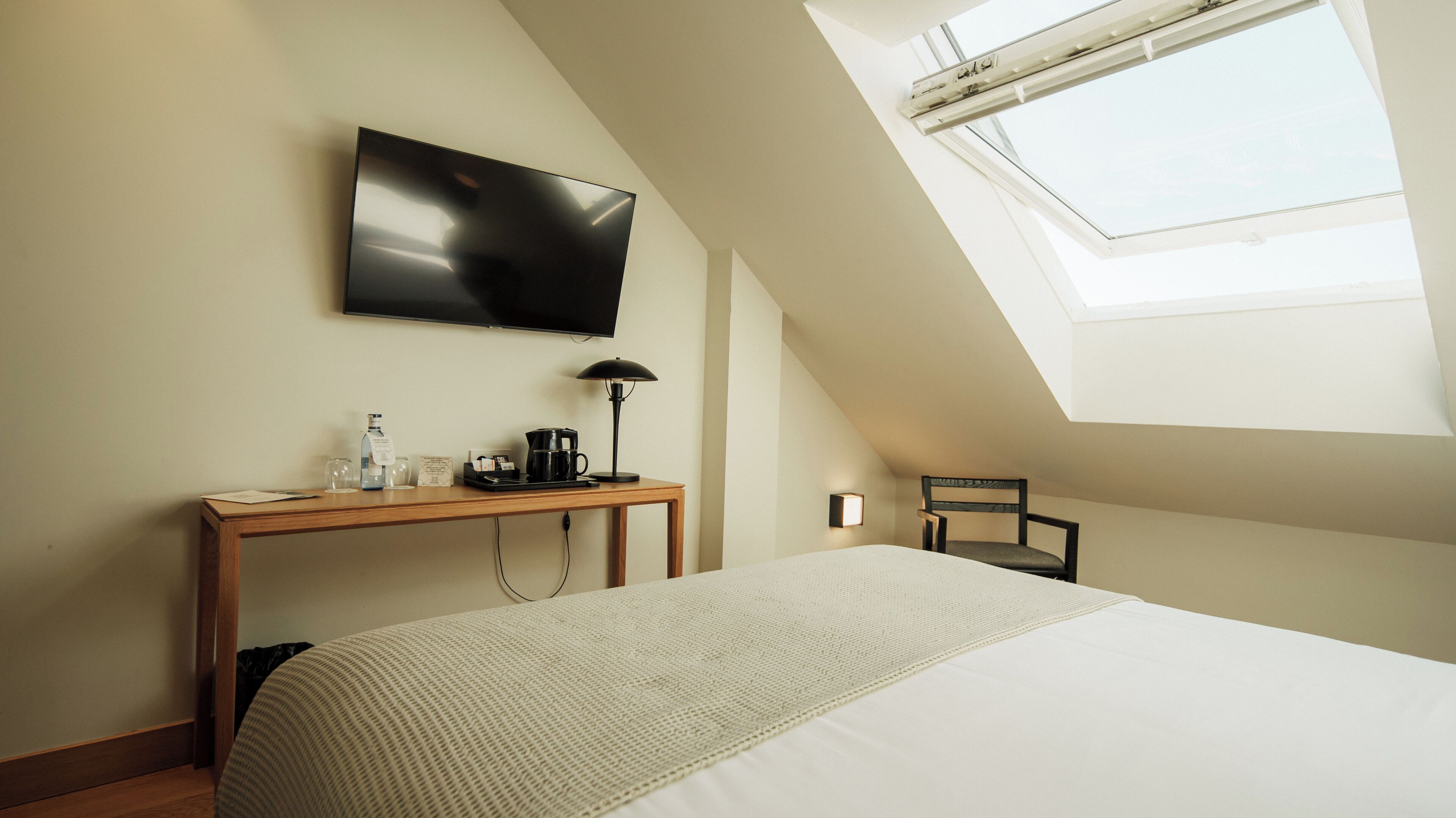 A hotel room with a bed, a desk with a flat-screen TV, a coffee maker, and a chair.
