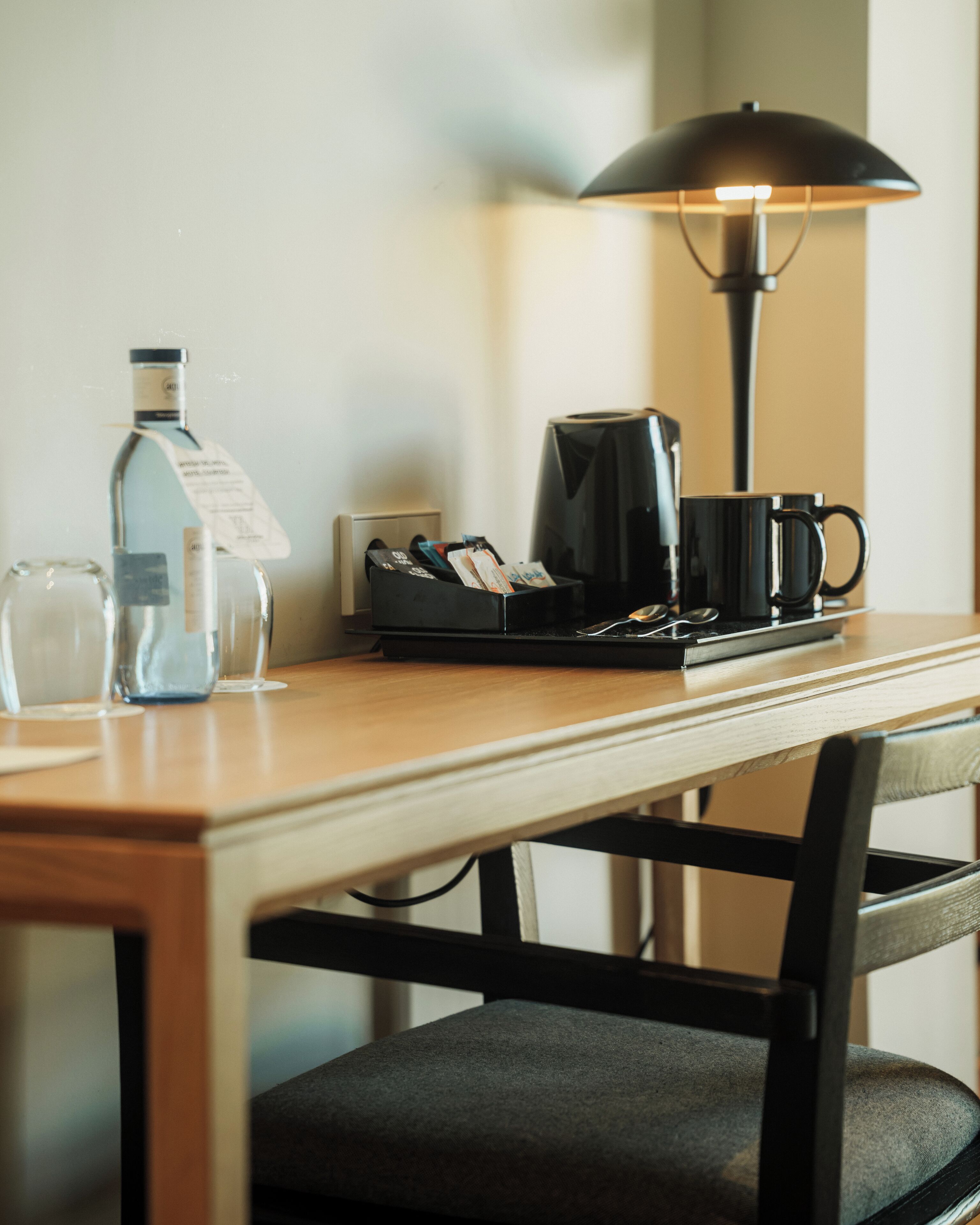 Une table en bois avec une machine à café, une lampe, une bouteille et une tasse.