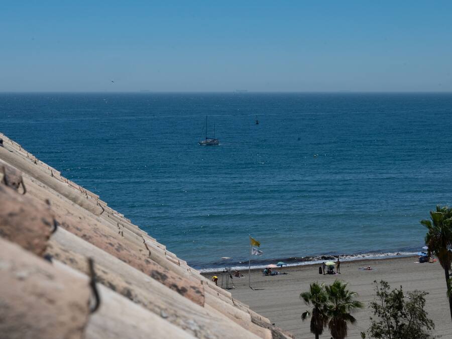 Una playa con costa rocosa, un velero en el agua y palmeras.