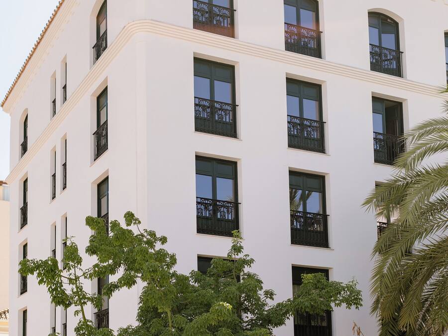 Un edificio de varios pisos con balcones, rodeado de abundante vegetación.