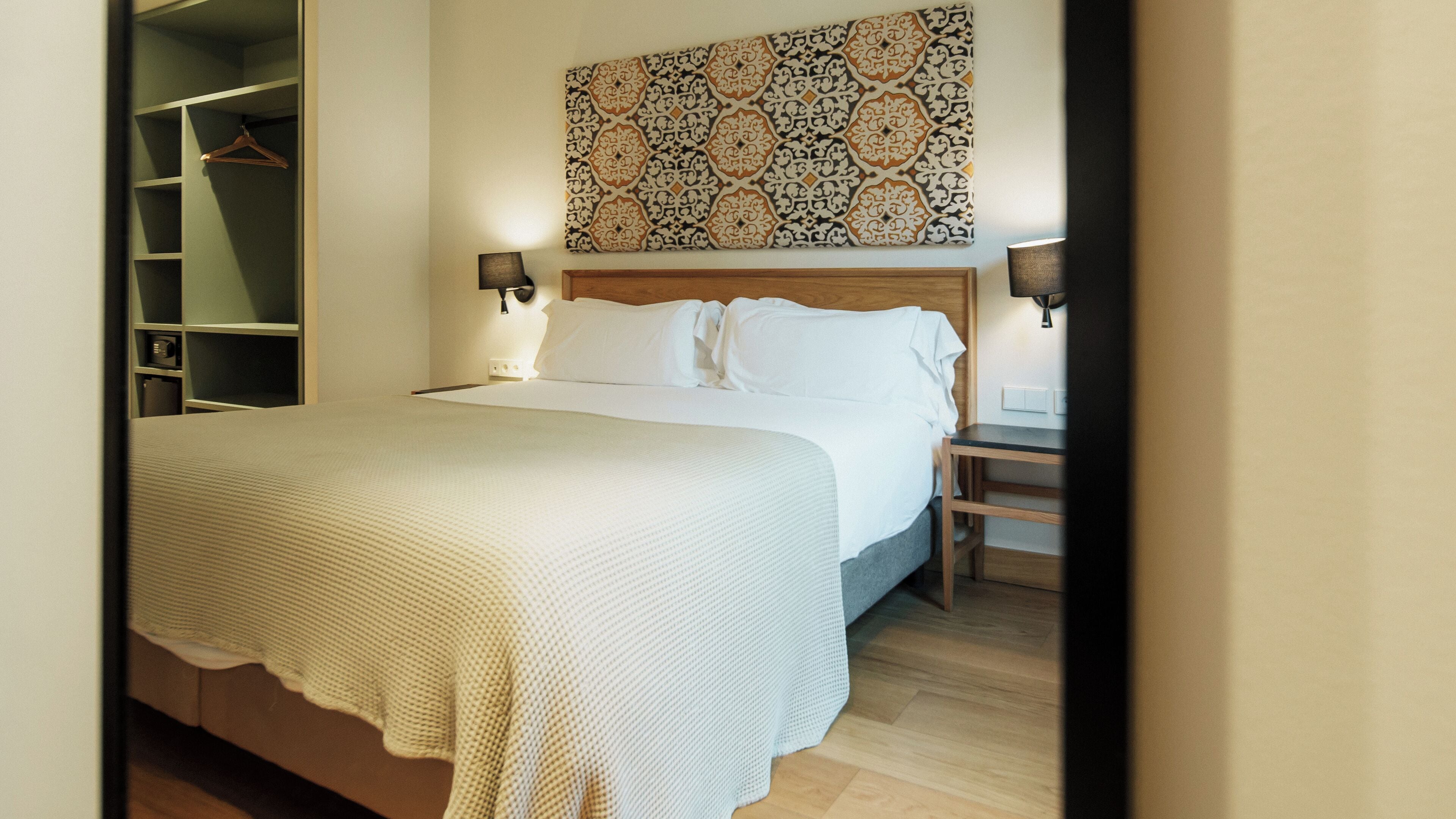 Un lit bien fait, avec du linge de lit blanc, une tête de lit en bois et deux lampes de chevet.