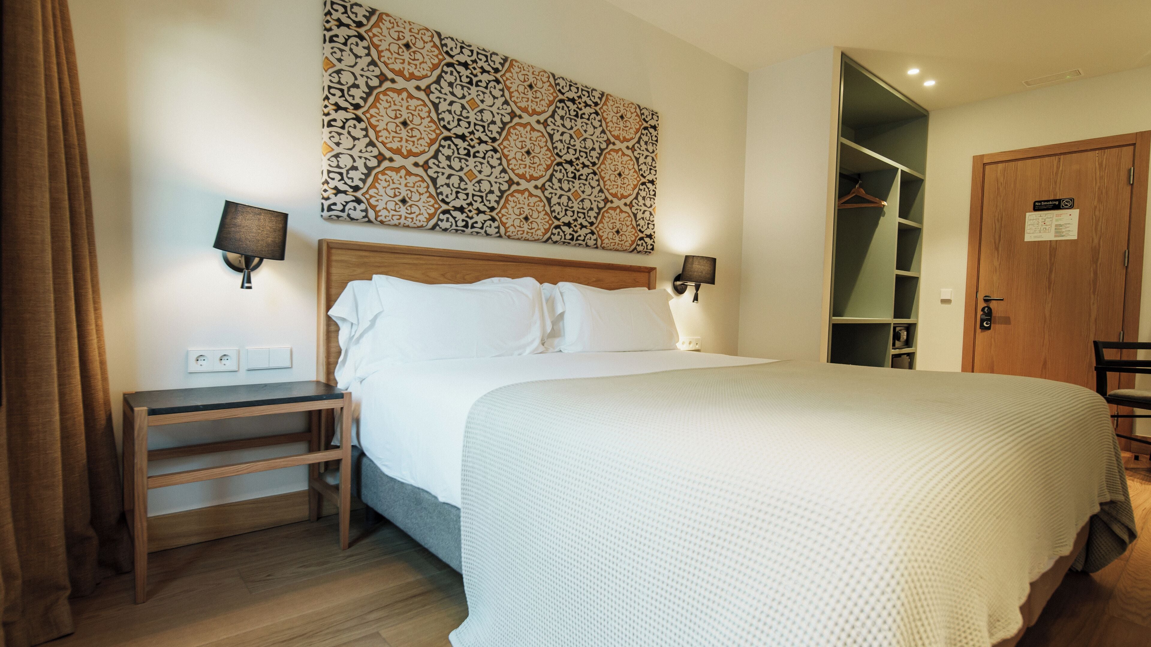 Una camera d'albergo ordinata con un letto grande, comodini, un armadio e un'opera d'arte appesa al muro.