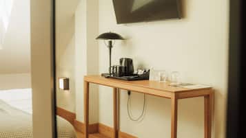 Habitación de hotel con cama, escritorio con lámpara, cafetera y televisor de pantalla plana en la pared.