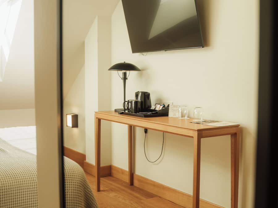 Habitación de hotel con cama, escritorio con lámpara, cafetera y televisor de pantalla plana en la pared.