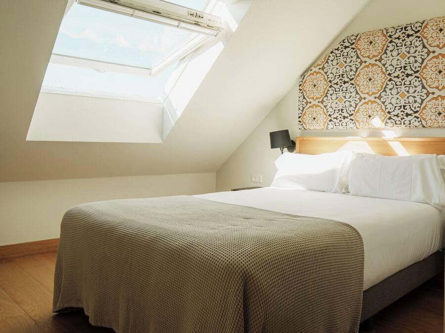 Ein Schlafzimmer mit Dachfenster, einem Bett mit weißen Leinen, einem gemusterten Kopfteil und Holzboden.