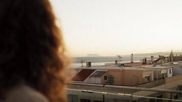 Vista desde un balcón sobre un paisaje urbano con edificios y una lejana vista al mar.