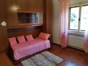 A bedroom with a bed, wooden wardrobe, window with curtains, radiator, and a rug. - Appartamento Nerio -avander House (Muggia)