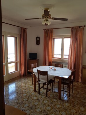A dining area with a table, chairs, a ceiling fan, and a television. - Appartamento Nerio -avander House (Muggia)