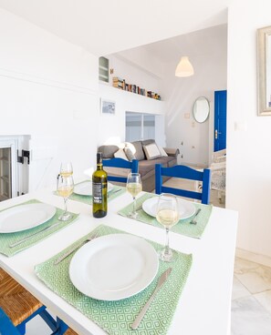 Un coin repas avec une table blanche dressée pour quatre personnes, une bouteille de vin et des verres.