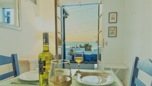A dining table set with a bottle of wine, a glass, and plates, with a view of the sea through an open door. - Beach House With Seaview (Naxos)