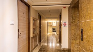 A hotel hallway with a wooden door labeled "301", a no-smoking sign, and an elevator with a digital display. - Treebo Fourth Avenue (Chennai)
