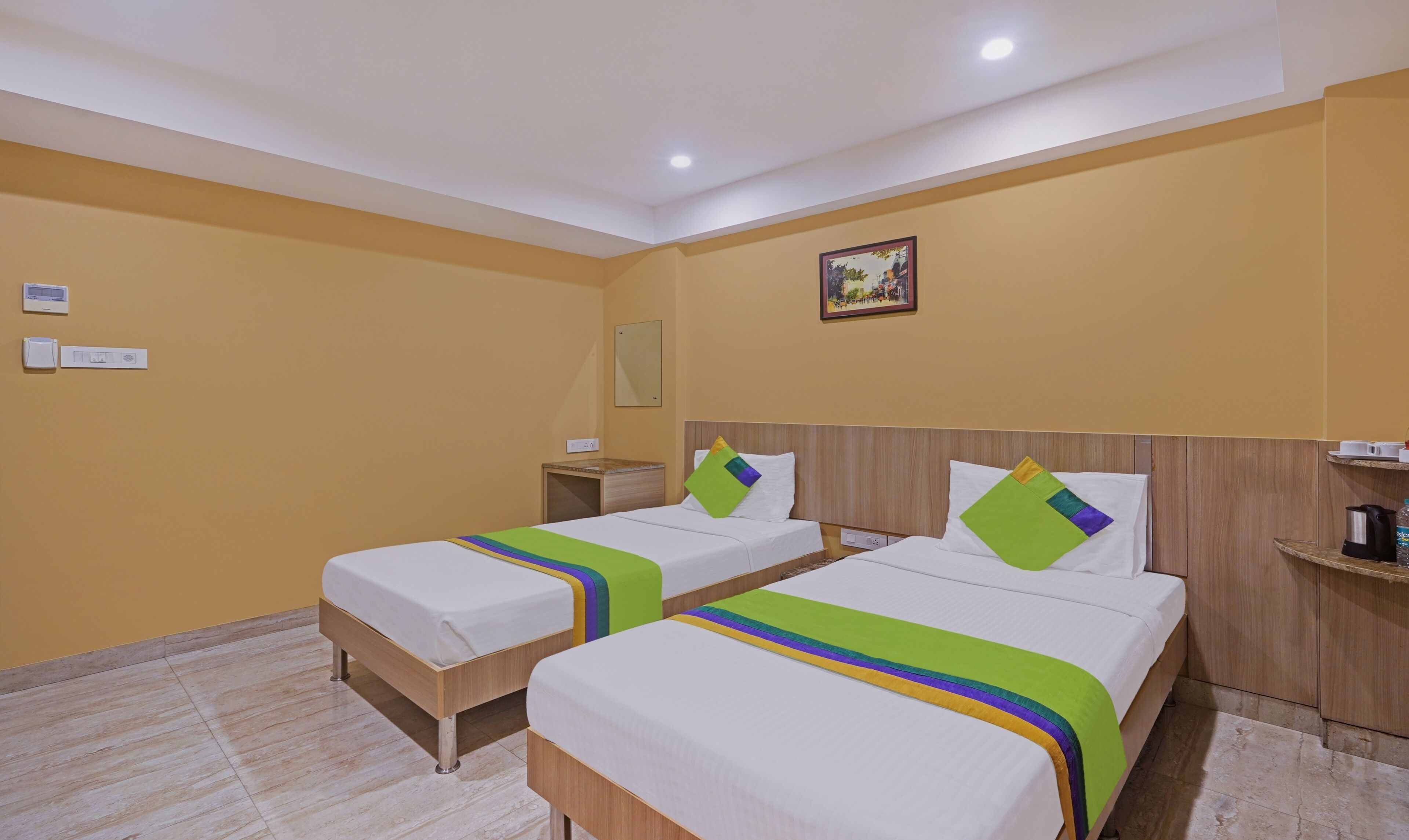 A hotel room with two beds, a nightstand, a wall-mounted heater, and a painting.