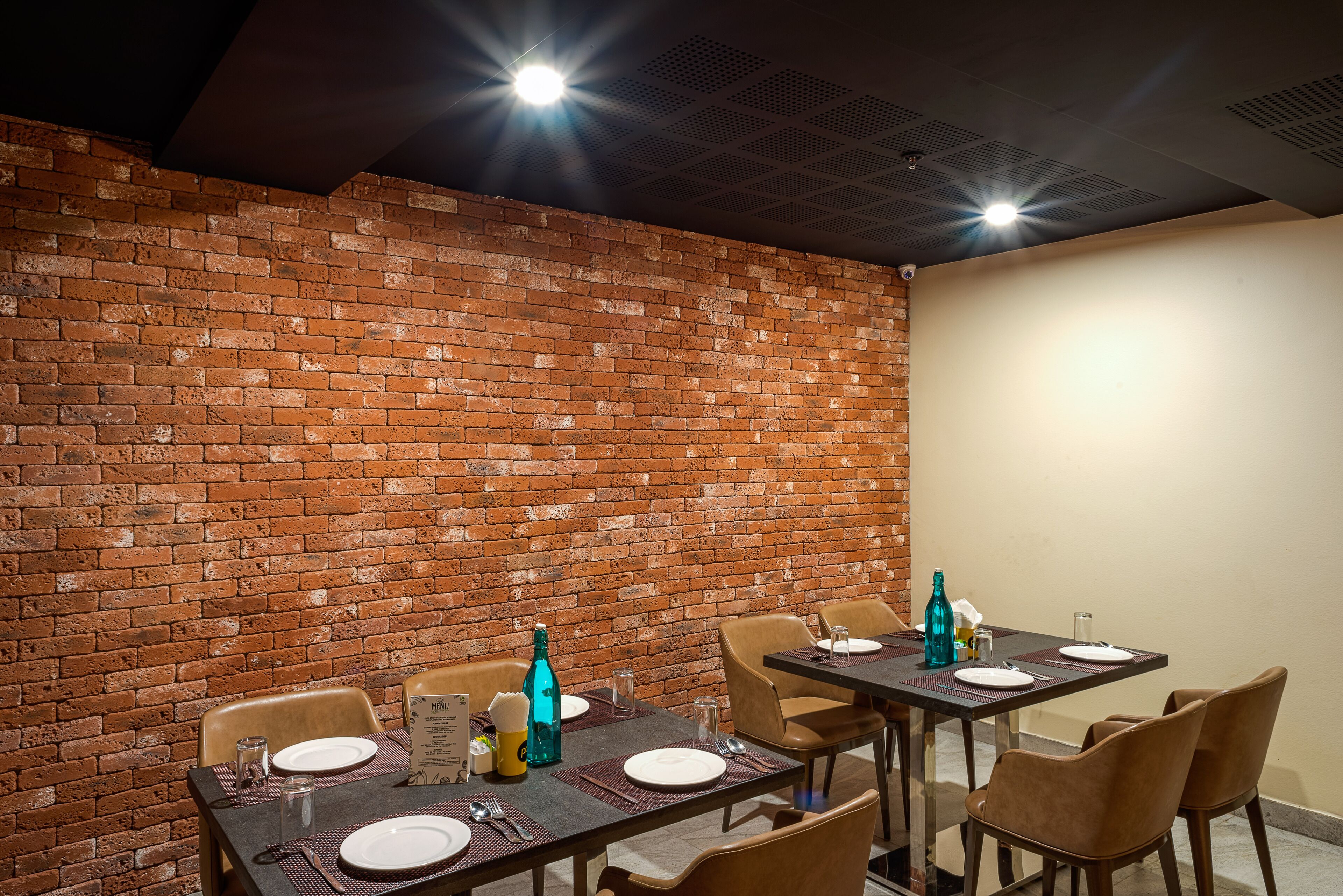 Un comedor con paredes de ladrillo, mesas dispuestas con platos, vasos y cubiertos.