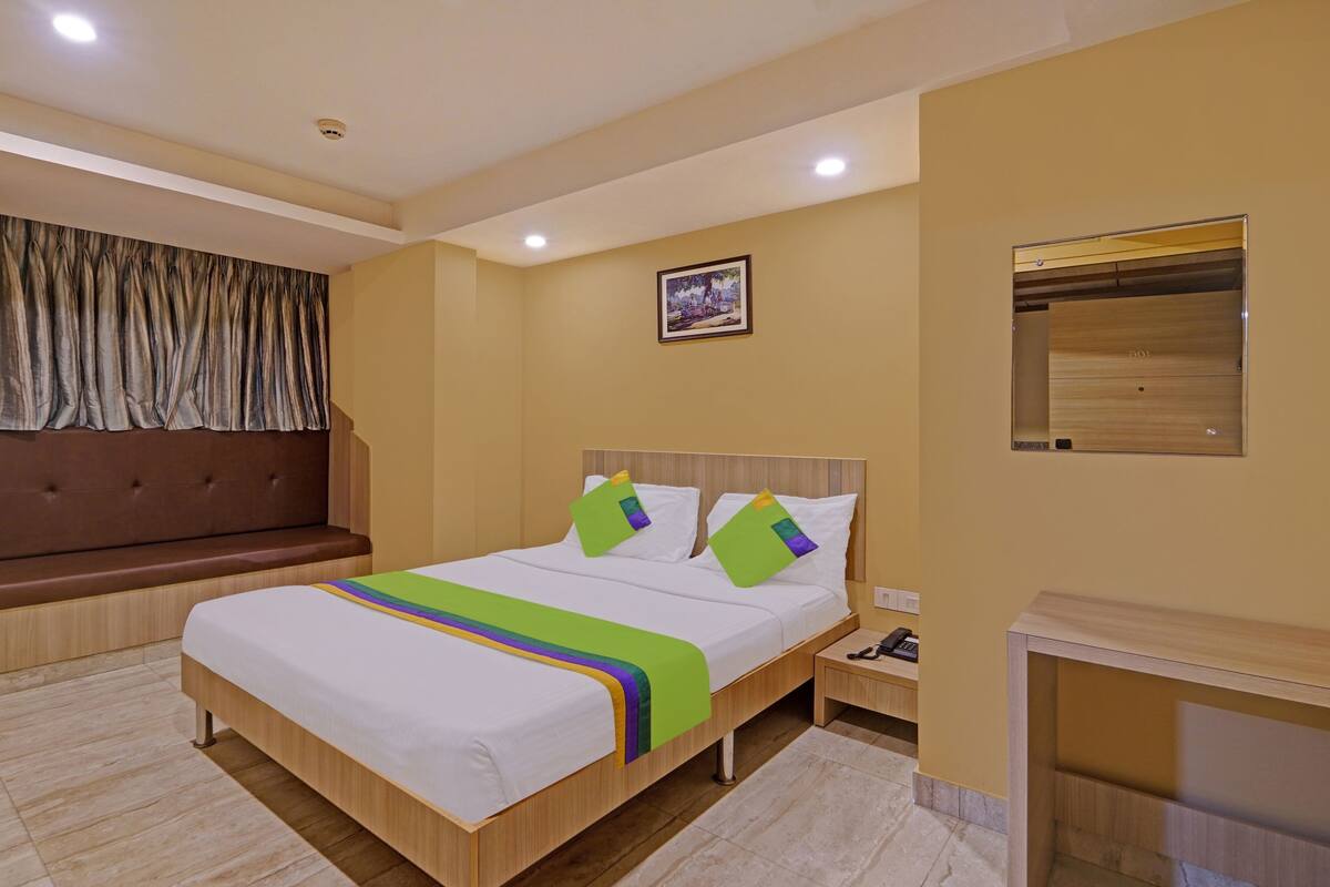 A hotel room with a bed, a bench, a bedside table, a mirror, and a picture on the wall.