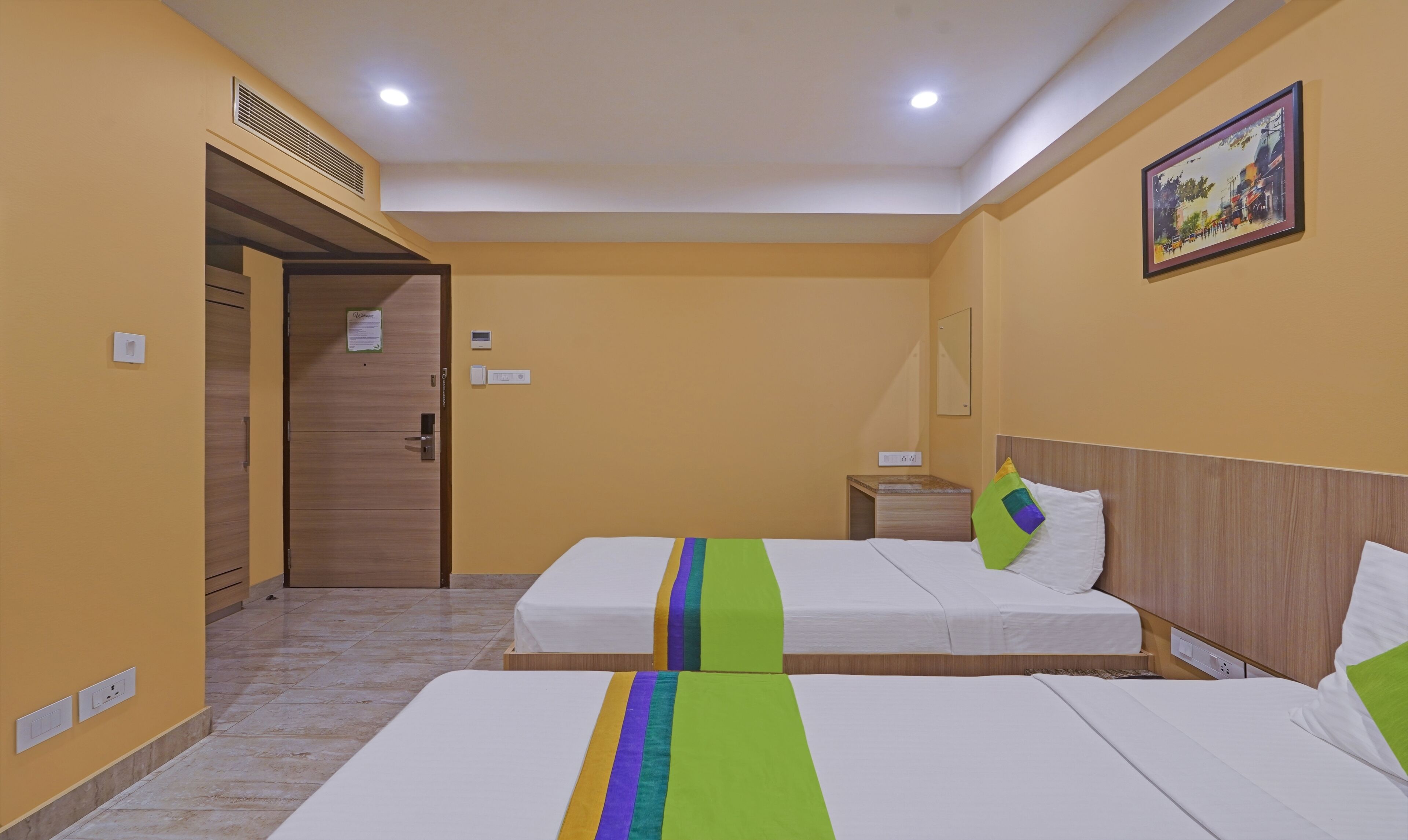 A hotel room with two beds, a wooden wardrobe, a nightstand, and a painting on the wall.