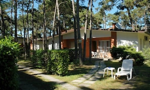 A bungalow with a patio, surrounded by trees and greenery.