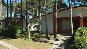 Um edifício de dois andares com fachada bege e detalhes em castanho, rodeado por árvores e vegetação.