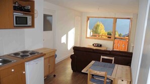 A compact kitchen with a microwave, stove, and dishwasher. There is a brown sofa and a small table with a chair. A window provides a view of the outdoors. - 2 Bed Apartment with great views backing onto the Diable ski lift (Les Deux Alpes)