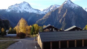 A building with a sloped roof, a parking lot, and mountains in the background. - 2 Bed Apartment with great views backing onto the Diable ski lift (Les Deux Alpes)