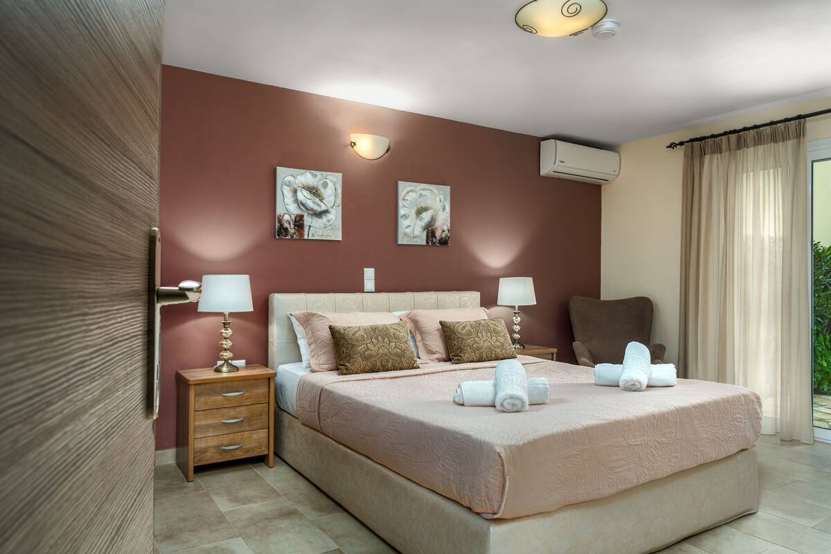 A bedroom with a large bed, two bedside tables with lamps, a chair, and artwork on the wall.