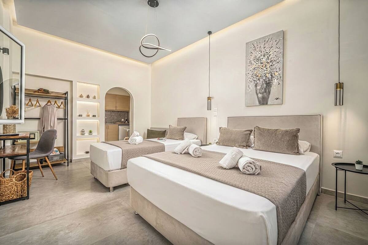 A modern hotel room with two beds, a sitting area, a kitchenette, and a large mirror.