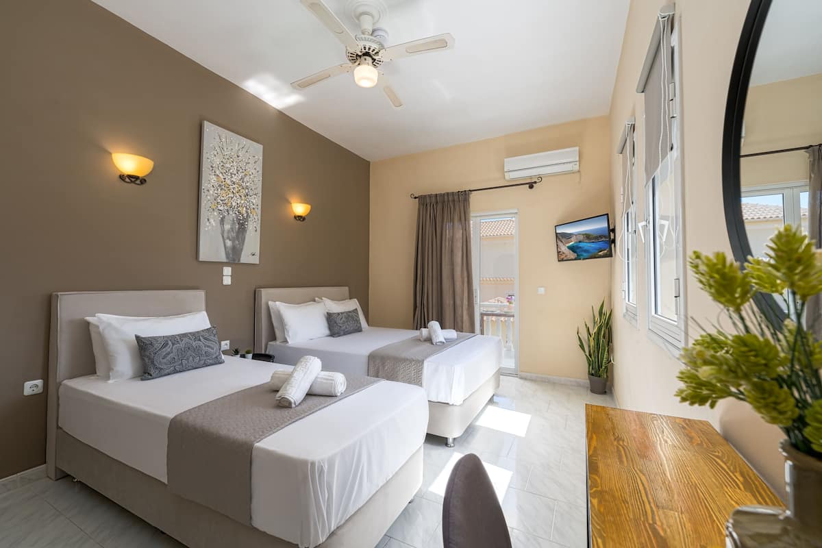 A hotel room with two beds, a ceiling fan, wall-mounted air conditioning, a TV, and a wooden table.