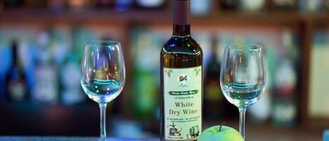 A bottle of White Dry Wine and two empty glasses on a bar counter with a blurred background of shelves.