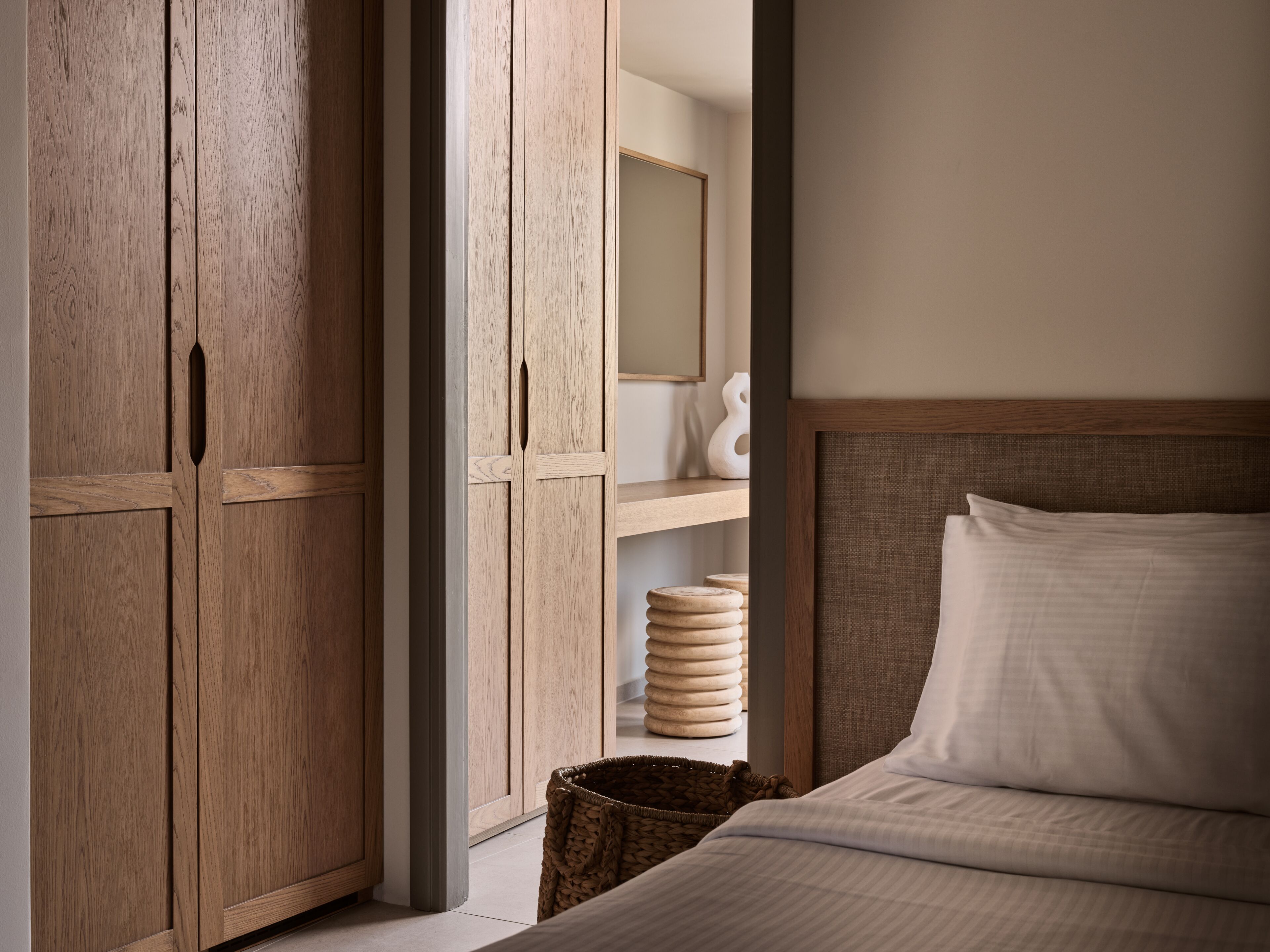 A bedroom with a wooden wardrobe, a bed with white bedding, and a woven basket on the floor.
