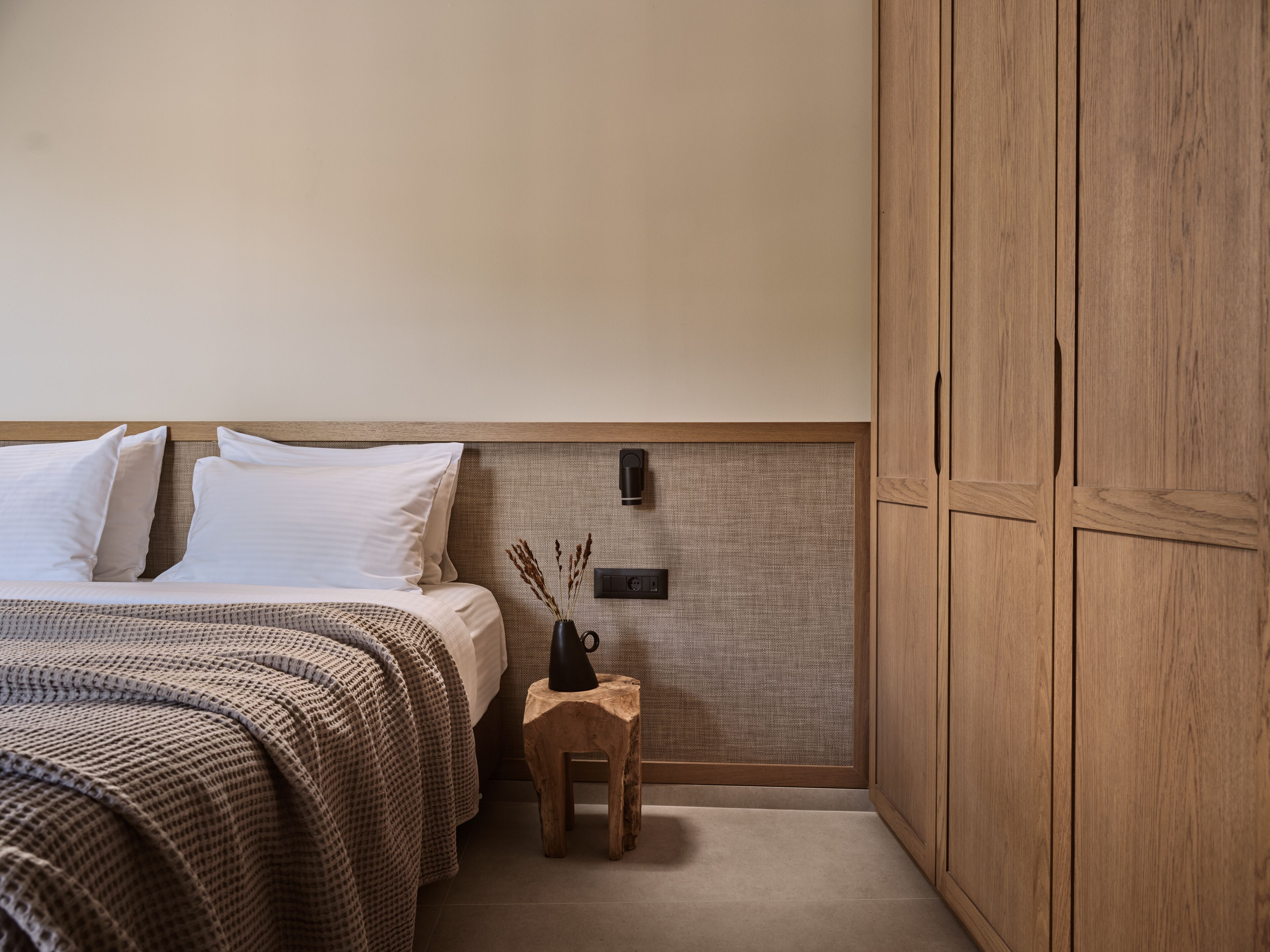 Ein Schlafzimmer mit einem Bett, einem Nachttisch, einem Holzschrank und einer Wandleuchte.