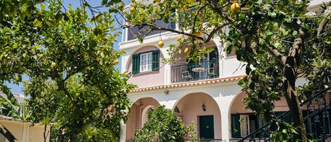 A building with a balcony, arched windows, and a garden area with various plants.