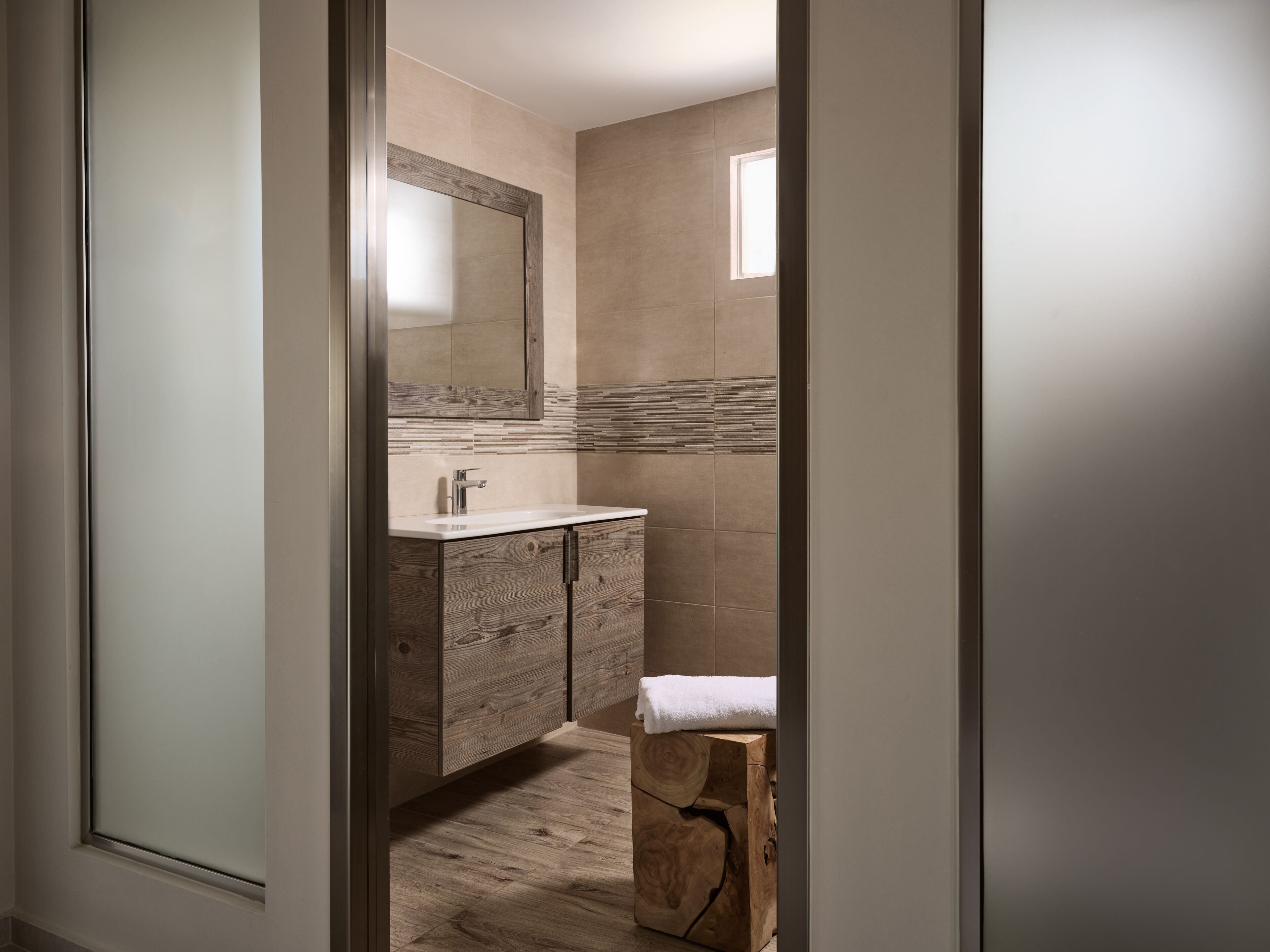 Une salle de bain moderne avec un meuble-lavabo en bois, un grand miroir et une petite fenêtre.