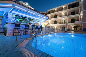 A swimming pool area with a bar and seating, surrounded by a multi-story building with balconies. - Alamis Hotel & Apartments (Zakynthos)