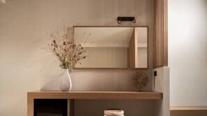 A minimalist wooden console table with a vase of dried plants, a round decorative object, and a mirror above it. - Alamis Hotel & Apartments (Zakynthos)