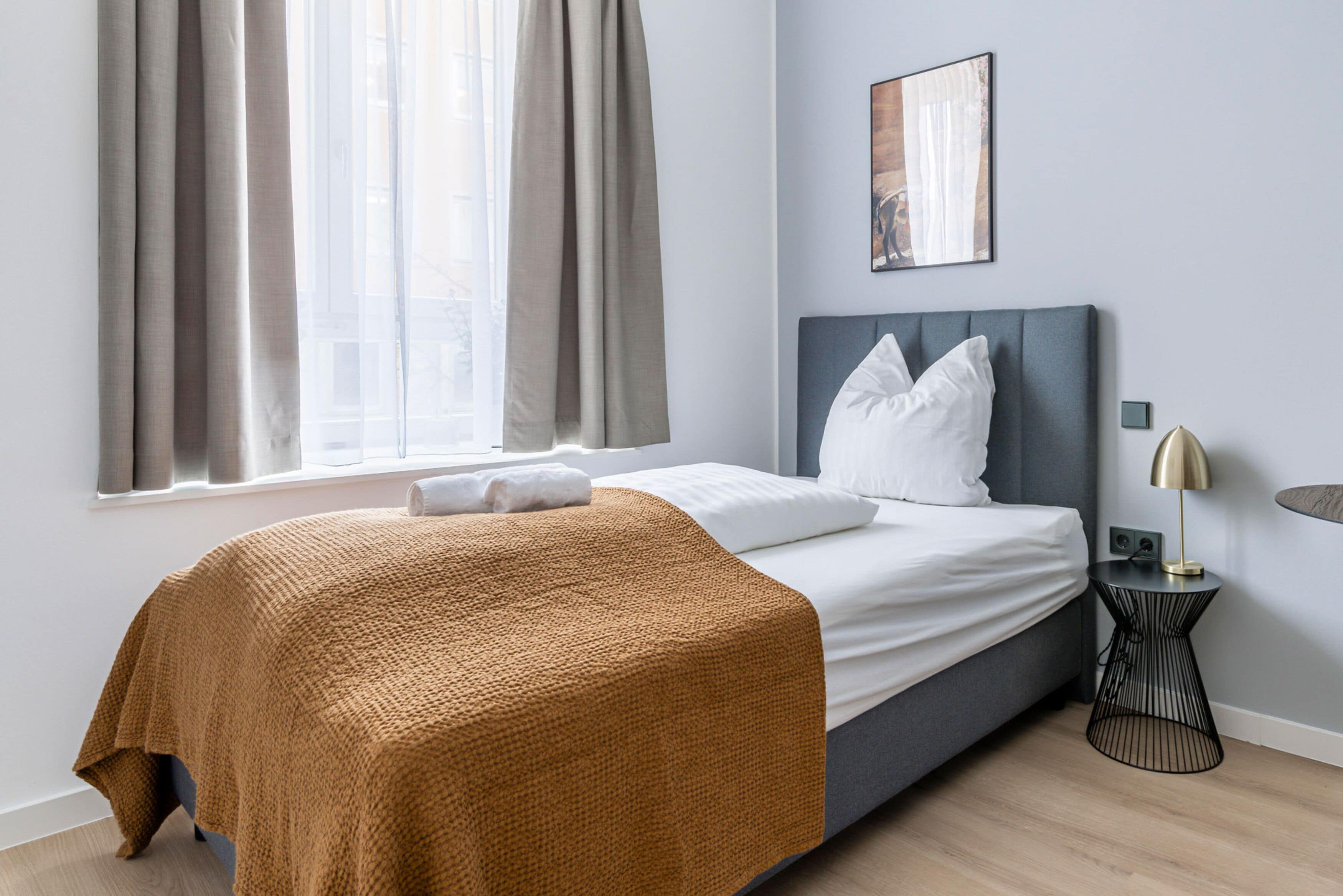 Una habitación de hotel moderna con cama, cortinas, una mesita de noche y un cuadro en la pared.