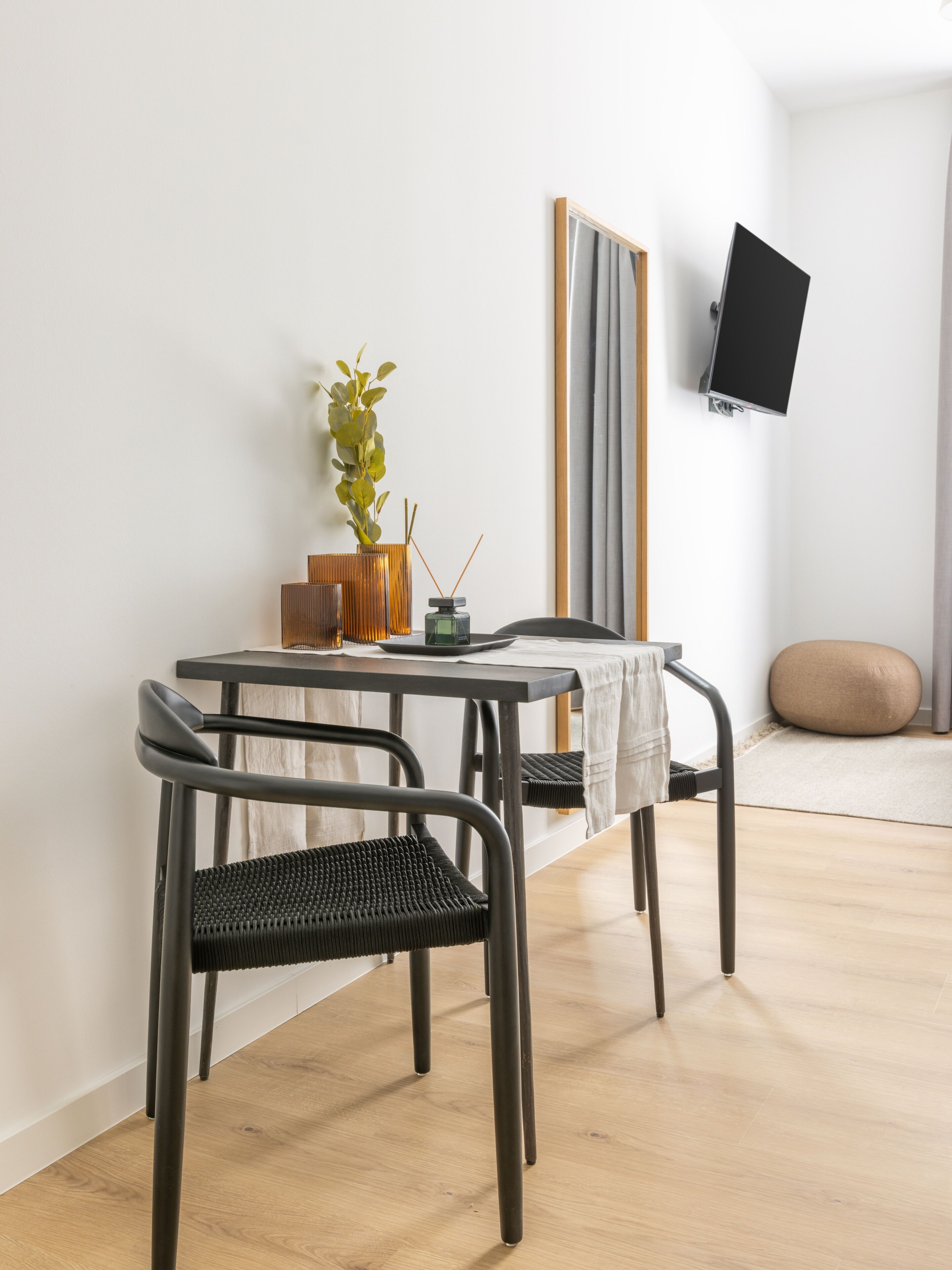 A modern dining area with a table, chairs, a plant, and a TV mounted on the wall.