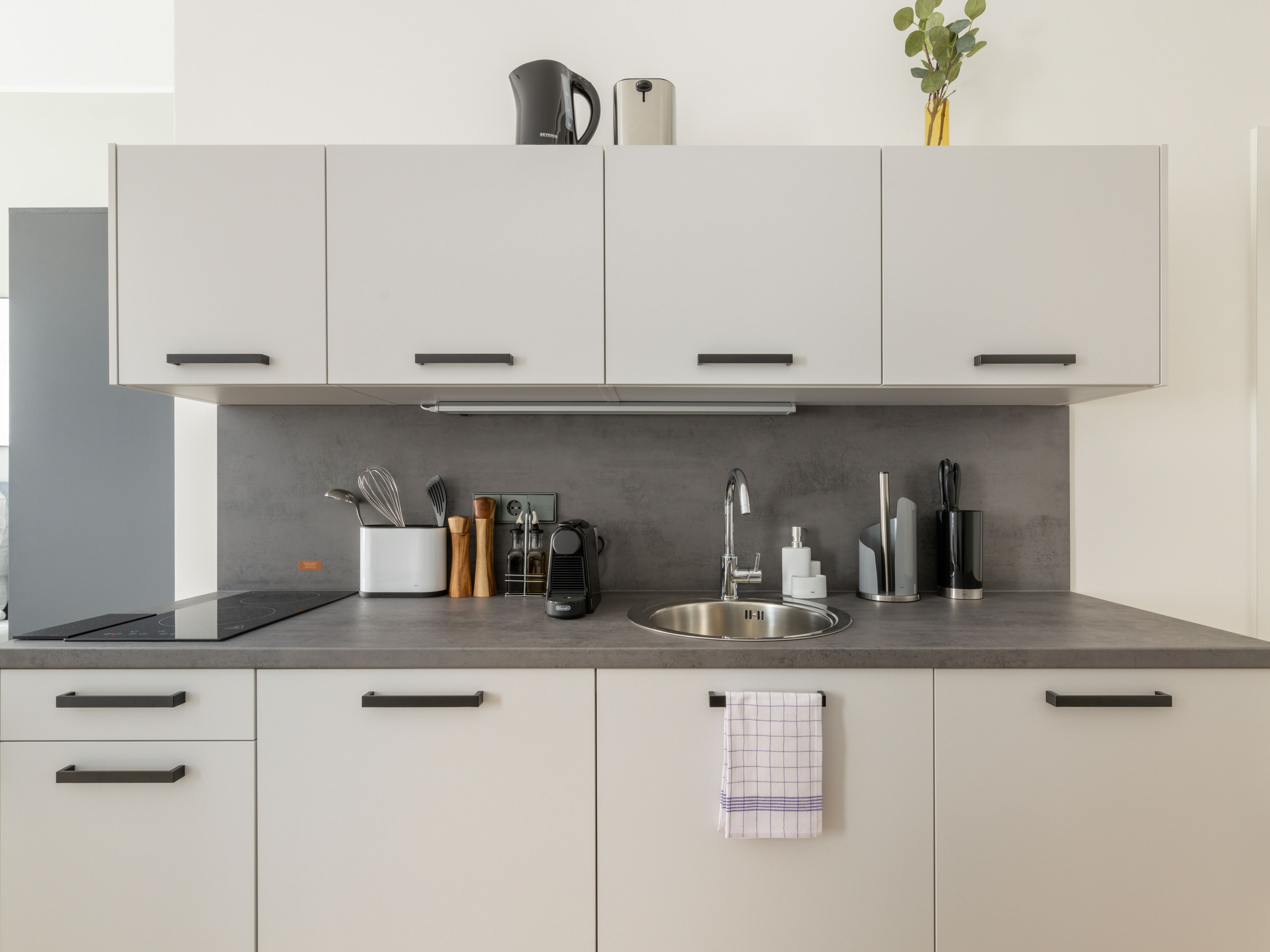 A modern kitchen with white cabinets, a stainless steel sink, and a coffee maker.